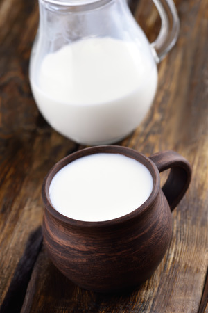 Milk in ceramic cup and glass jug on wooden tableの写真素材