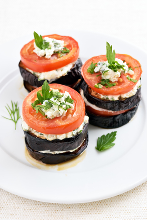 Eggplant, tomato and curd cheese stacks on white plateの写真素材