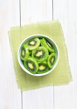 Kiwi slices in bowl over white wooden background, top viewの写真素材