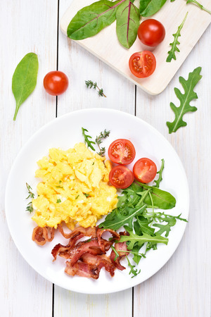 Breakfast with scrambled eggs, bacon and vegetable salad, top viewの写真素材