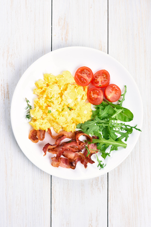 Scrambled eggs, bacon and vegetable salad on plate, top viewの写真素材