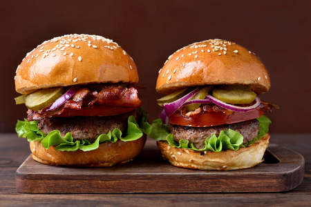 Homemade hamburger with beef, fried bacon, onion, tomato, lettuce and marinated cucumber on wooden board. Close up viewの写真素材