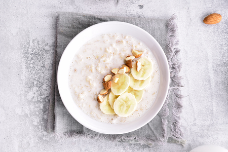 Oats porridge with banana slices and nuts in bowl over stone background. Top view, flat lay, close upの写真素材