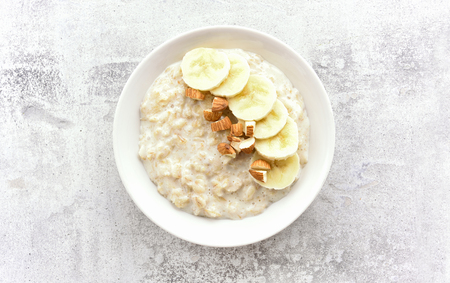 Oats porridge with banana slices and nuts in bowl over stone background. Diet healthy nutrition food concept. Top view, flat layの写真素材