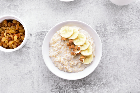 Oats porridge with banana slices and nuts in bowl over stone background. Dish for breakfast. Diet healthy nutrition food concept. Top view, flat lay.の写真素材