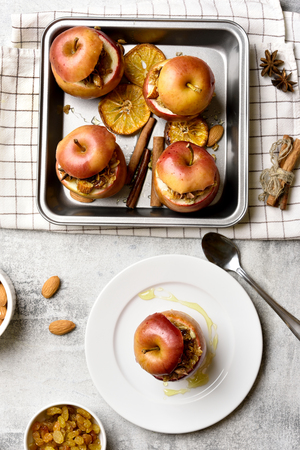 Red baked apples with granola, cinnamon, nuts and honey on stone background. Healthy vegetarian dessert. Top view, flat layの写真素材
