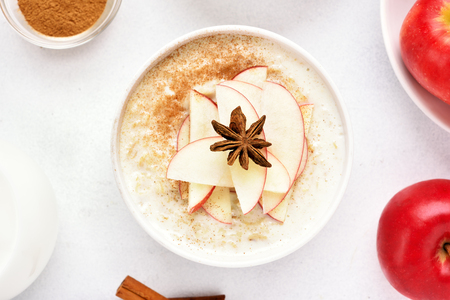 Oatmeal porridge with red apple slices and cinnamon on white stone background. Healthy diet breakfast concept. Top view, flat lay, close upの写真素材