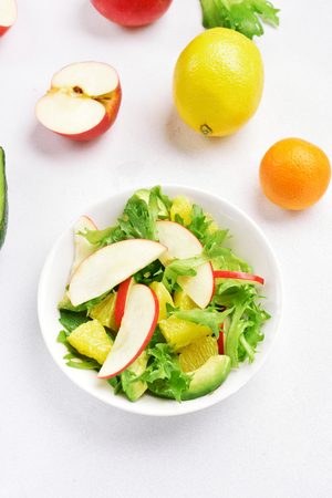 Natural organic food. Fruit vegetable salad with red apples, avocado, orange slices on white stone background. Healthy diet food. Top view.の写真素材