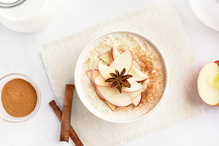 Oatmeal porridge with red apple slices and cinnamon. Healthy diet breakfast concept. Top view, flat layの写真素材