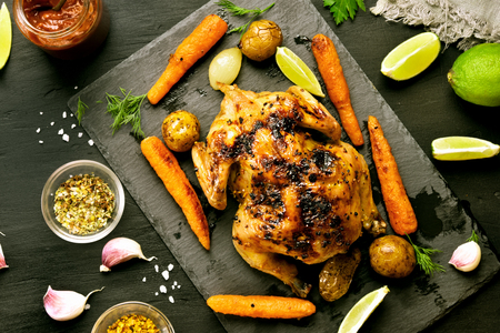 Grilled chicken with vegetables over black stone background. Top view, flat layの写真素材