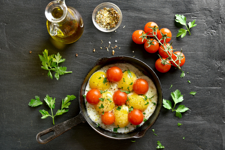 Fried eggs with tomatoes in frying pan on black stone background. Top view, flat layの写真素材