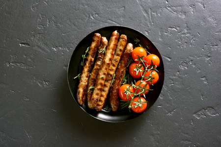 Grilled sausage and cherry tomatoes on plate over black stone background with copy space. Top view, flat layの写真素材