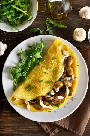 Omelette with mushrooms, chicken meat, greens on wooden table. Top view, flat layの写真素材