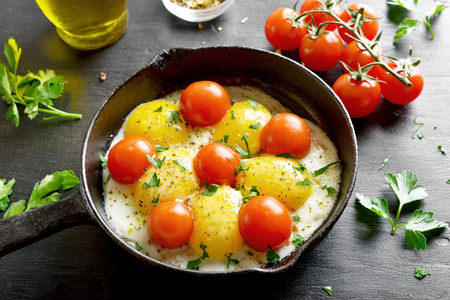 Fried eggs with tomatoes in frying pan on black stone tableの写真素材