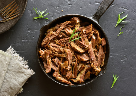 Slow cooked italian beef for sandwiches in frying pan on black stone background. Top view
