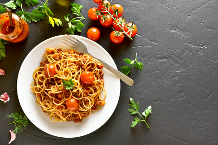 Spaghetti with minced meat and cherry tomatoes on black background with copy space. Top view, flat layの写真素材