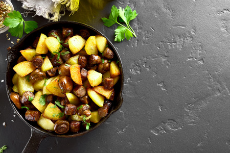 Roasted potatoes with mushroom and sausages in frying pan over black stone background with copy space. Top view, flat layの写真素材