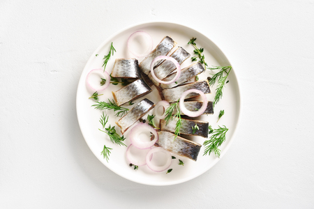 Salted herring fillet with spice, herbs and onion on plate on white stone background with copy space. Marinated sliced fish. Food with healthy unsaturated fats, Omega 3. Top view, flat layの写真素材