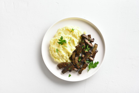 Roasted beef liver with mashed potatoes on white plate over stone background with copy space. Top view, flat layの写真素材
