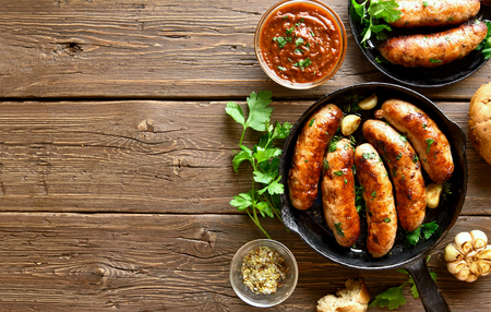 Sausages in frying pan and tomato sauce over wooden background with copy space. Top view, flat layの写真素材
