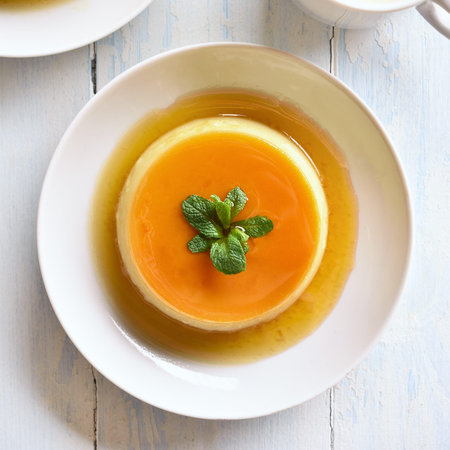 Close up of caramel custard pudding in bowl over wooden background. Top view, flat lay