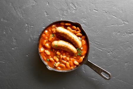 Grilled sausages with baked white beans in tomato sauce in frying pan over black stone background with copy space. Top view, flat layの写真素材