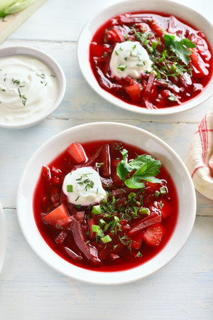 Russian ukrainian soup (borscht) with greens and sour cream. Beetroot soup in bowl on white wooden...