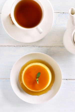 Caramel custard pudding and cup of tea on wooden background. Top view, flat layの写真素材