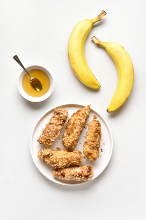 Tasty deep fried bananas on plate over white stone background. Dessert from pan fried bananas in asian style. Top view, flat layの写真素材
