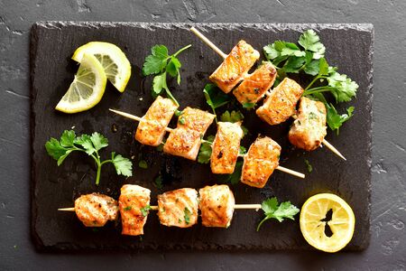Barbecue salmon skewers on slate board over black stone background. Top view, flat layの写真素材
