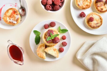 Cottage cheese pancakes, fritters with fresh raspberries on plate over light stone background. Top view, flat layの写真素材