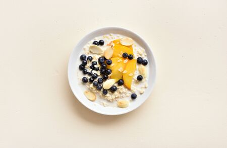 Oats porridge with peach slices, almond and wild blueberries in bowl over light stone background with free space. Healthy diet breakfast concept. Top view, flat layの写真素材