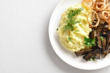 Close up of mashed potatoes with roasted beef liver on plate over white stone background. Top view, flat layの写真素材
