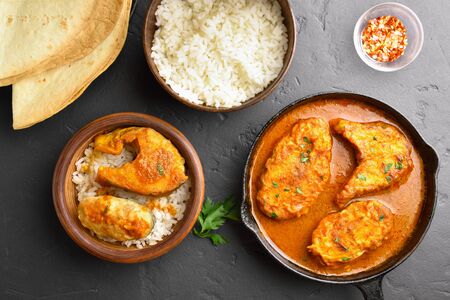 Fish curry with rice in wooden bowl on black stone table. Indian style food. Top view, flat layの写真素材