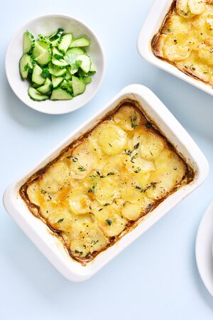 Vegetarian food concept. Potato gratin in baking dish and cucumber salad over blue stone background. Top view, flat layの写真素材