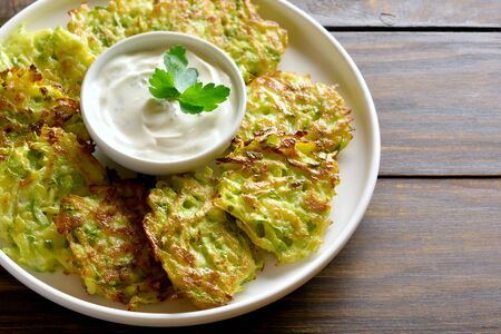 Close up of zucchini fritters with sauce on white plate over wooden table. Vegetarian food. の写真素材