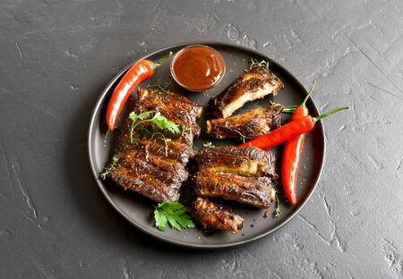 Spicy grilled spare ribs on plate over black stone background. Tasty bbq meat. の写真素材