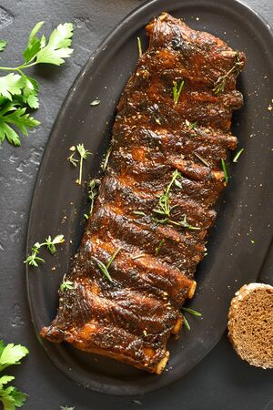 Close up of grilled spare ribs on plate over black stone background. Tasty bbq meat. Top view, flat layの写真素材