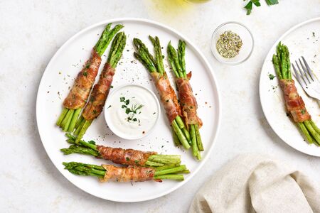Tasty bacon wrapped asparagus on white plate over light stone background. Top view, flat layの写真素材