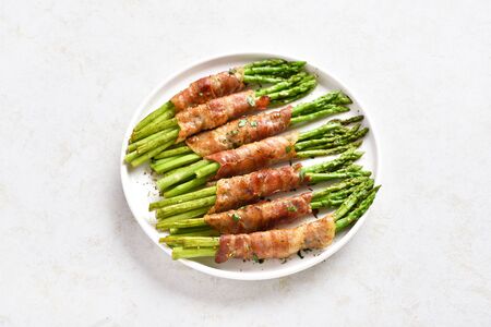 Close up of bacon wrapped asparagus on white plate over light stone background.の写真素材