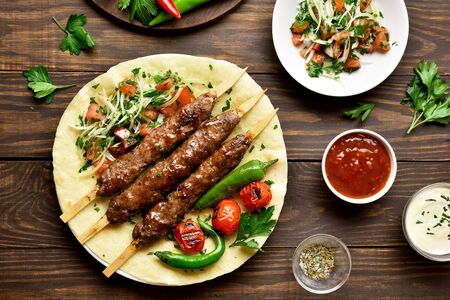 Tasty turkish Adana Kebab with fresh vegetables on flatbread over wooden background. Top view, flat layの写真素材