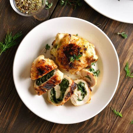Stuffed chicken fillet with spinach and cheese on white plate on wooden table. Top view, flat layの写真素材