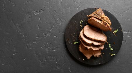 Sliced grilled roast beef on wooden board over black stone background with free space. Top view, flat layの写真素材