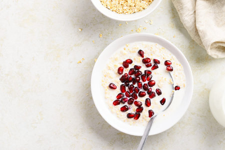 Oatmeal porridge with pomegranate seeds in bowl over light stone background with free text space....