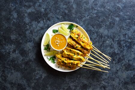 Grilled chicken skewers served with peanut dipping sauce. Chicken satay with peanut sauce. Tasty meal for dinner or party appetizers. Blue stone background with free text space. Top view, flat layの写真素材