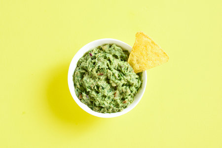 Guacamole dip in bowl over yellow background with free text space. Healthy avocado spread. Top view,...