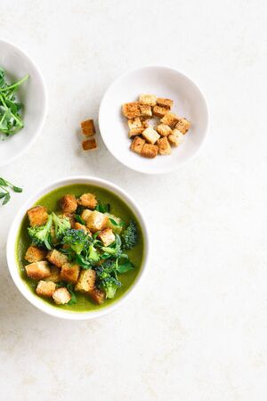 Healthy broccoli green pea cream soup with croutons in bowl over light stone background with free text space. Diet detox food concept. Top view, flat layの写真素材