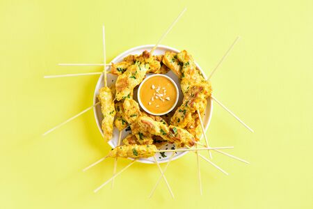 Grilled chicken skewers served with peanut dipping sauce. Chicken satay with peanut sauce. Tasty meal for dinner or party appetizers. Yellow background, top view, flat lay, close upの写真素材