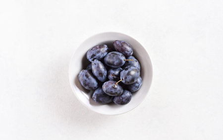 Fresh ripe plums in bowl over white background with free text space. Top view, flat lay
