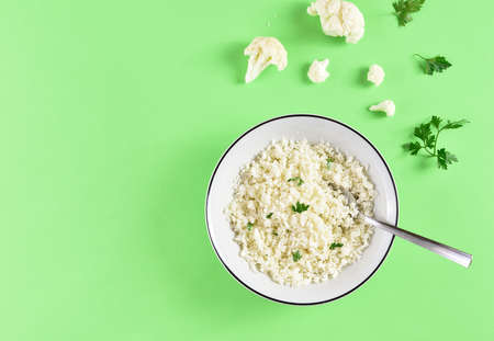 Cauliflower rice in a bowl on green background with free text space. Top view, flat layの写真素材